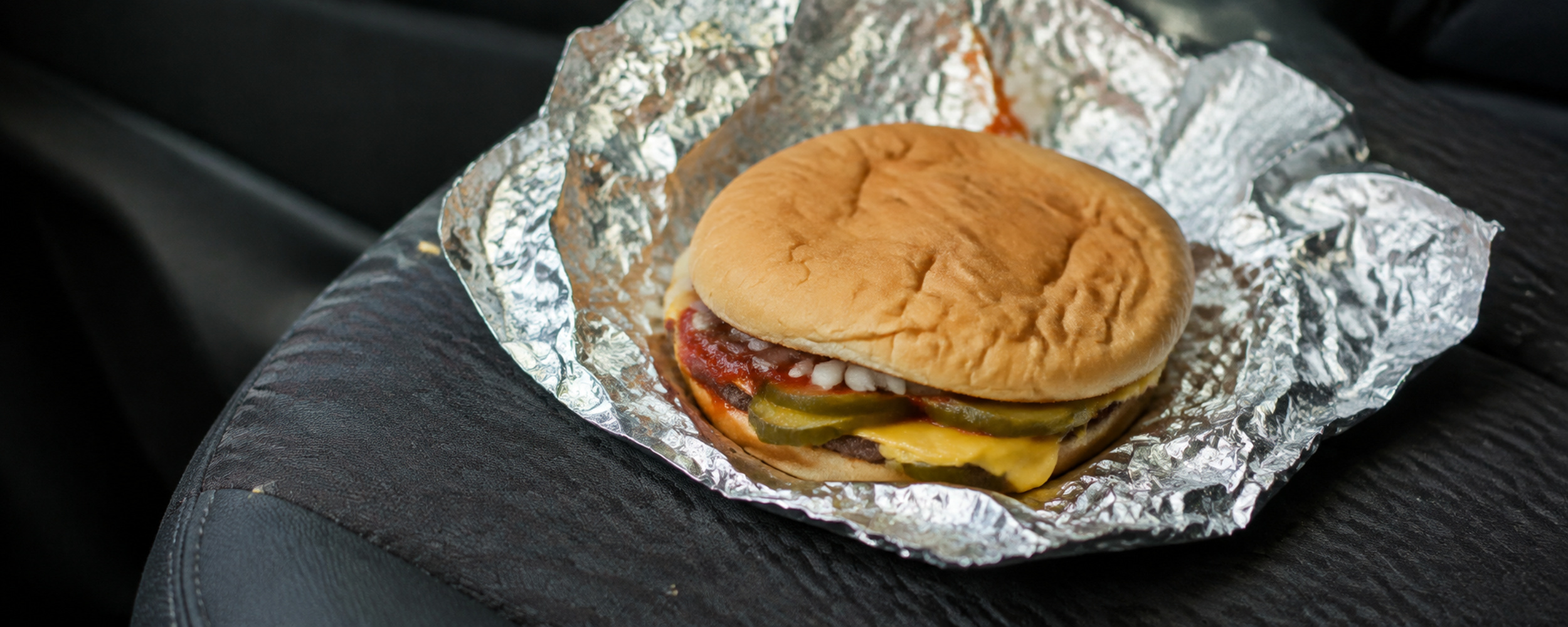 A foil-wrapped griddled burger with pickles